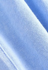 Tissu bleu clair à la texture douce, présentant un motif tricoté et des variations subtiles de teinte, mettant l'accent sur la douceur et un tissage uniforme.