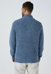 Zils adīts džemperis ar struktūru ribu dizainu, augstu apkakli un garām piedurknēm. Redzamas šuves un nedaudz elastīga auduma. Aizmugures skats.