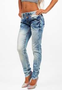 Jeans in denim azzurro fitted con cuciture a contrasto, design a cinque tasche, accessori in oro e una leggera scoloritura verso le cosce.