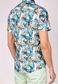 Chemise à manches courtes avec un fond blanc et un motif vibrant de feuilles de palmier vertes et dorées. Tissu léger avec une coupe décontractée.