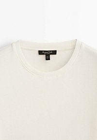 Valkoinen ribbattu puuvillapaita, jossa on pyöreä kaula-aukko. Sisältää mustan etiketin, jossa on brändin nimi ja kokotiedot. Pehmeä tekstuuri, yksinkertainen muotoilu.