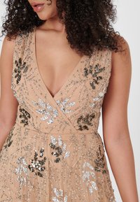 Beaded evening dress w kolorze nude, z głębokim dekoltem w kształcie V, skomplikowanym haftem w srebrze i czerni, z kwiatowymi wzorami oraz miękką, płynącą fakturą.