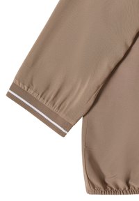 Manche et côté d'une veste beige avec des poignets élastiques et une bande blanche sur le poignet sur fond blanc.