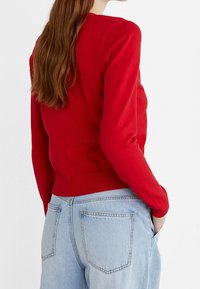Rode gebreide trui met lange mouwen, ronde halslijn en ribbelzoom, gecombineerd met lichtblauwe high-waisted jeans met achterzakken.
