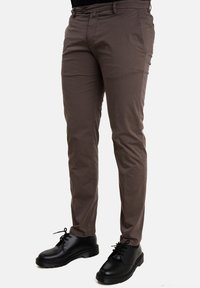Chino marroni realizzati in tessuto misto cotone, design slim fit, davanti piatto e tasche laterali, abbinati a scarpe nere stringate.