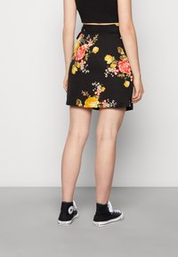 Saia preta floral com padrões de rosas amarelas e vermelhas, design justo e um ligeiro evasê. Usada com ténis altos pretos.