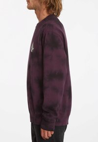 Lila tie-dye sweatshirt med rund halsringning, ribbade muddar och en liten logotyp-patch på bröstet. Tillverkad av mjukt tyg.