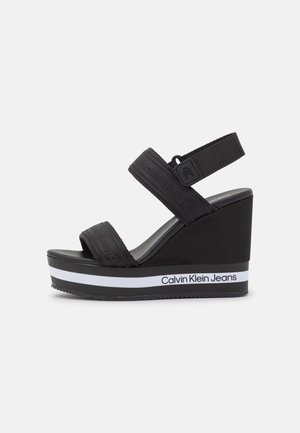 Sort kile-sandal med to justerbare stofremme og Calvin Klein Jeans branding på den hvidstribede platformsål.