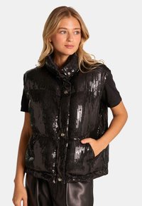 Schwarzige Pailletten-Weste mit hohem Kragen, Druckknopfverschluss und Seitentaschen. Glatte Textur mit glänzendem Finish, ideal zum Layering.