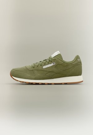 Low-Top olivgrüner Wildleder-Reebok-Sneaker mit weißer Sohle und Gummiaußensohle, mit Schnürverschluss und Branding an der Seite und an der Ferse.