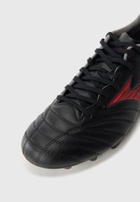 Black synthetic soccer cleat featuring textured surface, red accents, black laces, and a rounded toe design.