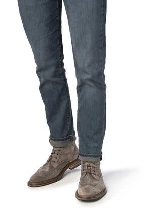Bottines en daim gris avec des détails brogues, associées à un jean bleu foncé retroussé. Les bottines sont dotées d'une semelle en bois et de lacets plats.