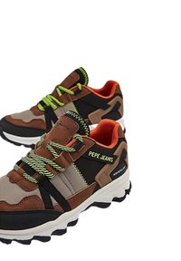 Zapatillas deportivas marrones y negras con cordones verdes, con una parte superior de tela texturizada y una marca audaz en el lateral. Suela blanca gruesa.