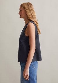 Marineblauw mouwloos topje met een losse pasvorm, ronde halslijn, zichtbare naden en licht textiel. G gedragen met lichtblauwe jeans.