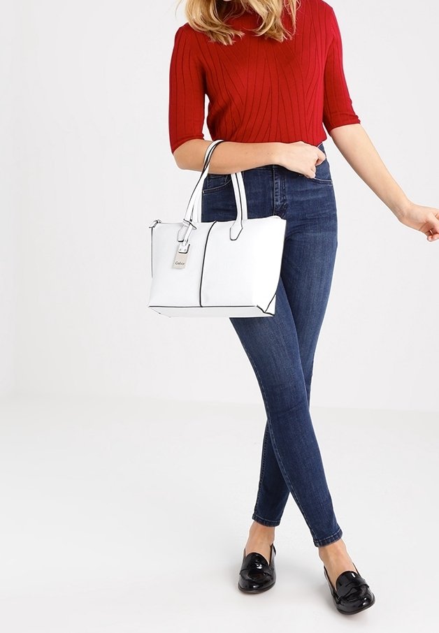 Witte handtas met zwarte accenten, gestructureerd ontwerp en twee bovenhandvatten, gecombineerd met strakke donkerblauwe jeans en een rode geribde trui.