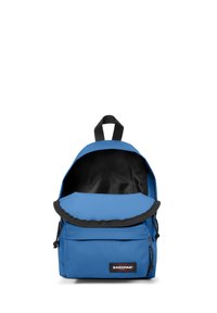 Blue fabric backpack with a rounded top, black lining, zippered front pocket, logo label, and adjustable black straps. Interior shows storage space.
