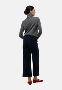 Pull à col roulé gris, pantalon large en velours côtelé bleu marine, ballerines rouges. Matériaux texturés ; design décontracté avec poches à l'arrière du pantalon.