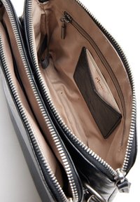 Interno di una borsa in pelle nera con rivestimento beige; presenta più scomparti e chiusure con zip; include uno slot per carte e una piccola borsa con zip.