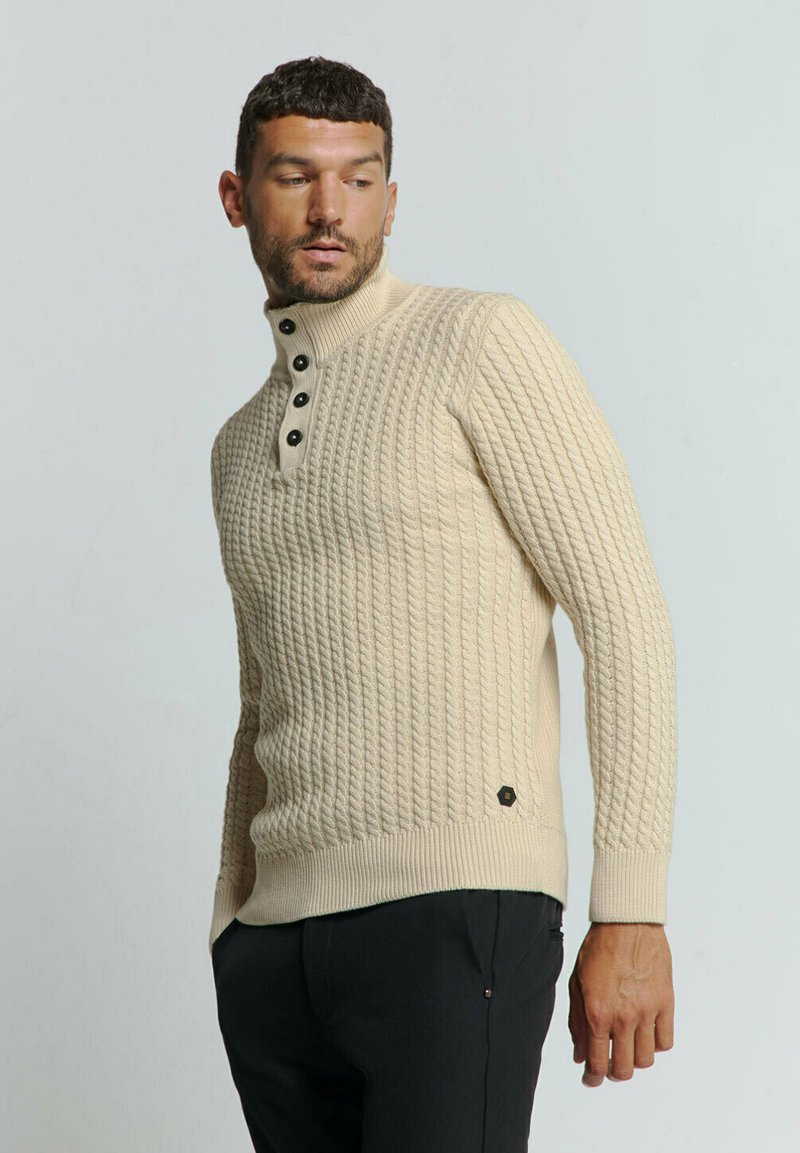 Beige gebreide trui met een hoge kraag, vier zwarte knopen, geribbelde manchetten en een klein logoaccent aan de zoom.