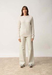 Vaalean beige raidallinen neulepaita pitkillä hihoilla, yhdistettynä vaaleanvihreisiin leveisiin housuihin ja harmaisiin kengiksi, joissa on kamouflagekuvio.