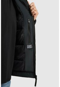 Czarna kurtka puchowa z podszewką, wyposażona w kieszeń na zamek i metkę z napisem "Khujo Original Changing Threads" w białym kolorze.