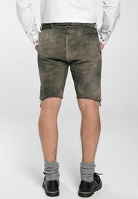 Dunkelgraue Shorts mit strukturierter Oberfläche, versehen mit einer knöpfbaren Seitentasche und umgeschlagenem Saum. Kombiniert mit schwarzen Schuhen und grauen, gestrickten Socken.