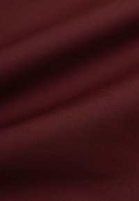 Bordowy materiał o gładkiej teksturze, z lekkim połyskiem i miękkim układzie, zaprezentowany w zbliżeniu, podkreślającym jego bogactwo.