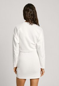 Vestido de sudadera blanco, tejido ligero, mangas largas, cintura ajustada, largo por encima de la rodilla, presenta aberturas laterales para facilitar el movimiento.