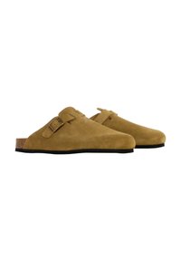 Sabots en daim d'une couleur beige chaud, avec un accent de boucle unique, une semelle en liège et une semelle en caoutchouc texturée noire.