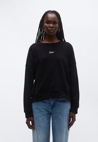 Μαύρο φούτερ με ριχτούς ώμους και ριμπ μανσέτες. Διαθέτει κεντημένο λογότυπο "BOSS" σε λευκό στο στήθος. Συνδυασμένο με ανοιχτό μπλε τζιν.