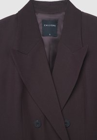 Dark brown double-breasted blazer with wide notch lapels and two visible black buttons, featuring Calliope brand label and size S inside collar.