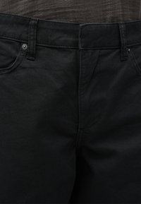 Κοντινή λήψη της μέσης μαύρου τζιν παντελονιού με θηλιές για ζώνη, φερμουάρ και κούμπωμα με κουμπί.