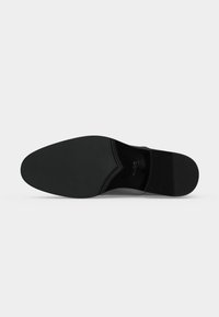Semelle d'une chaussure de ville noire formelle avec des parties en caoutchouc lisses et texturées sur un fond gris clair uni.