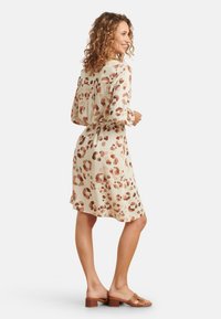 Leopardenmusterkleid in hellem Beige mit braunen Akzenten, gestaltet mit langen Ärmeln und einer fließenden Silhouette, kombiniert mit braunen Sandalen.