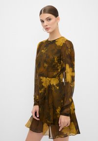 Bruine bloemenjurk met lange doorschijnende mouwen, een getailleerde taille en een uitlopende zoom. Bevat gele bloempatronen en een lichtgewicht, vloeiende stof.