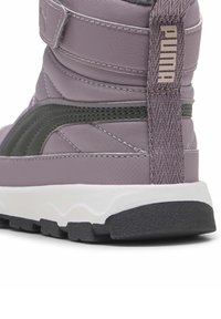 Lyse lilla støvle med en tekstureret overflade, sort accentstribe og hvid mellemsål. Har et logo bagpå og mønstret stropdetalje.