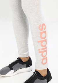 Szare legginsy ze dużym różowym logo "adidas" po boku. Połączone z czarnymi i szarymi butami sportowymi z zamkiem błyskawicznym.