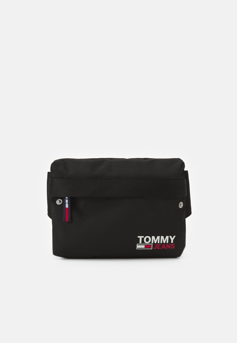 Borsa a tracolla nera in tessuto con chiusura a pattina, caratterizzata da un logo "TOMMY JEANS" in argento e un piccolo tag di accento rosso, bianco e blu sul lato.