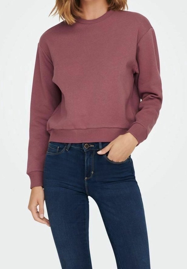 Femme portant un sweat-shirt mauve à manches longues et un jean bleu foncé taille haute, avec une main dans sa poche.