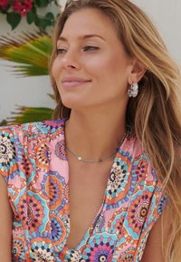 Colorful blouse with a vivid mandala pattern in pink, orange, and turquoise. Accessories include textured silver earrings and a delicate silver necklace.