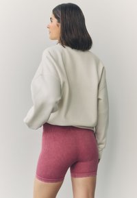 Sudadera crema extragrande con hombros caídos, combinada con pantalones cortos ajustados y acanalados de color burdeos. Textura de tela suave, diseño minimalista.