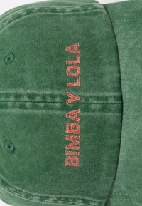 Roheline närvesaad cap punase broderdatud "BABY ALOHA" tekstiga eespaneelil, näidates kangast tekstuuri ja õmblusdetailide lähedalt.