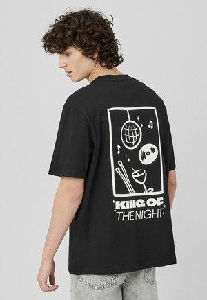 T-shirt en coton noir avec un grand motif blanc représentant une boule disco, des notes de musique et un verre, décoré de l'inscription « ROI DE LA NUIT ».