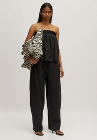Zwart strapless top met gerimpelde halslijn, gecombineerd met losse zwarte broek. Model houdt een tas met zebra-patroon vast. Gladde stof, minimalistisch ontwerp.