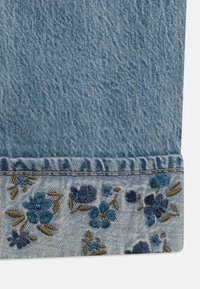 Denimová tkanina s přeloženým lemem, zdobená modrými a hnědými květinovými vyšíváními podél okraje.