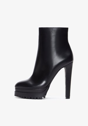 Bottines à talons hauts en cuir noir avec une plateforme épaisse et une semelle robuste, présentant une texture lisse et un design épuré et minimaliste.