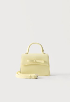 Petit sac à main jaune pastel avec poignée supérieure, un simple détail de nœud sur le rabat avant et une bandoulière amovible avec boucle.