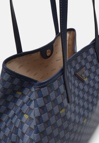 Granatowa torebka zgeometrycznym wzorem w odcieniach niebieskiego i szarości, z złotym zapięciem na zatrzask, dwoma uchwytami oraz wewnętrznym nadrukiem z logo.