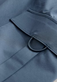 Texturiertes marineblaues Gewebe mit glatter Oberfläche, ausgestattet mit einer Klappentasche und einem Schlaufen-Detail zum Schließen. Einfaches Design, nahtlose Nähte.