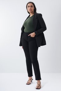 Blazer negro ajustado sobre un body verde oscuro, combinado con pantalones negros de corte slim y sandalias de tacones negros con tiras. Tejido liso y corte.